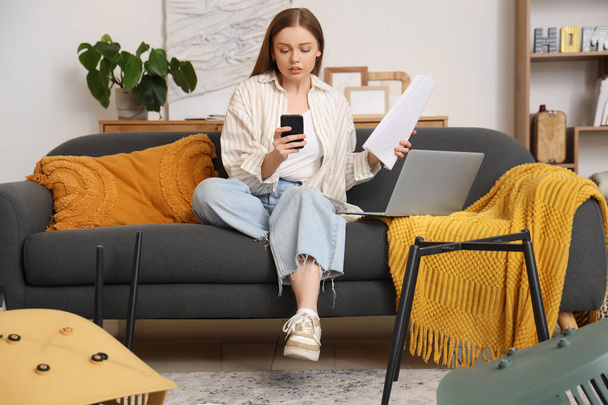Mooie jonge vrouw met handmatige, mobiele telefoon en laptop monteren meubels thuis - Foto, afbeelding