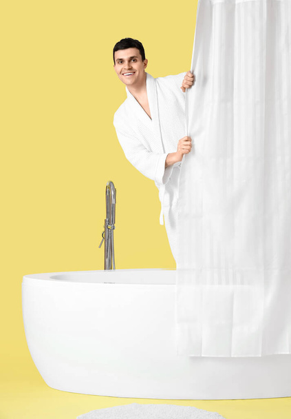 Jongeman in bad achter gordijn op gele achtergrond - Foto, afbeelding