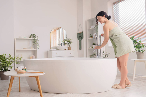Hermosa mujer con toalla de agua corriente en la bañera en casa - Foto, imagen