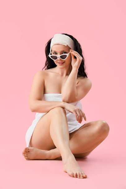 Young woman in towel with sunglasses sitting on pink background - Photo, Image