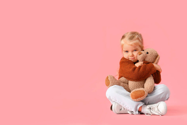Klein meisje met autistische stoornis knuffelen speelgoed beer op roze achtergrond - Foto, afbeelding