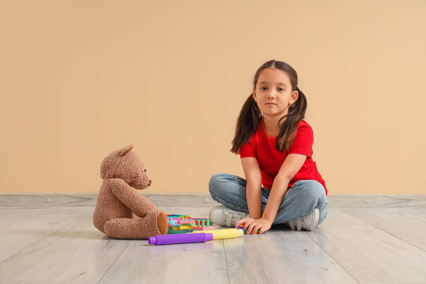 Маленька азіатська дівчинка з аутистичним розладом та іграшками, що сидять біля бежевої стіни - Фото, зображення
