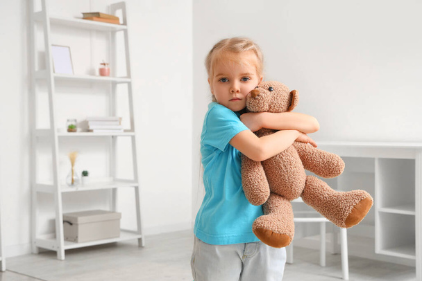 Маленькая девочка с аутизмом обнимает игрушечного медведя дома - Фото, изображение