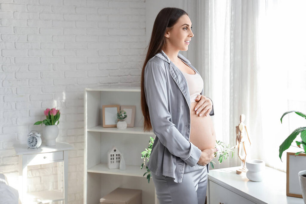 Mujer embarazada joven cerca de la ventana en el dormitorio - Foto, imagen