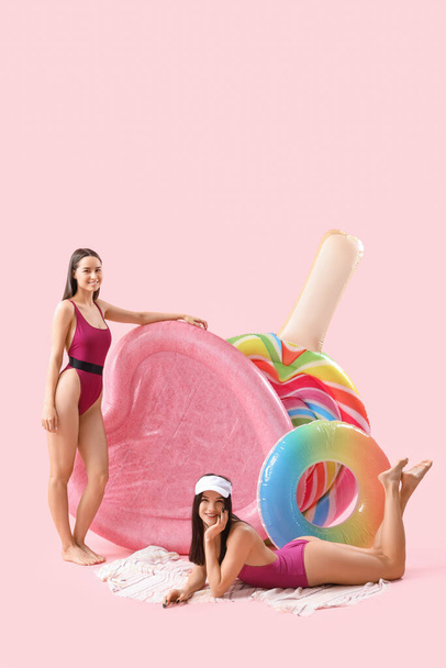 Amigas en ropa de playa con colchones de baño sobre fondo rosa - Foto, Imagen