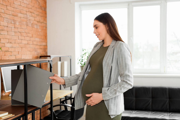 Donna d'affari incinta che prende cartella dallo scaffale in ufficio - Foto, immagini