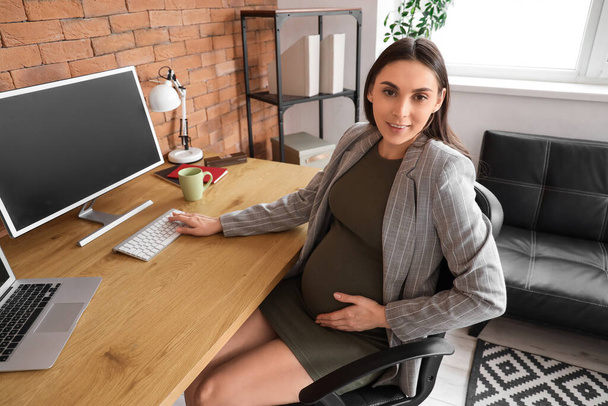 Embarazada mujer de negocios trabajando con la computadora en la mesa en la oficina - Foto, Imagen