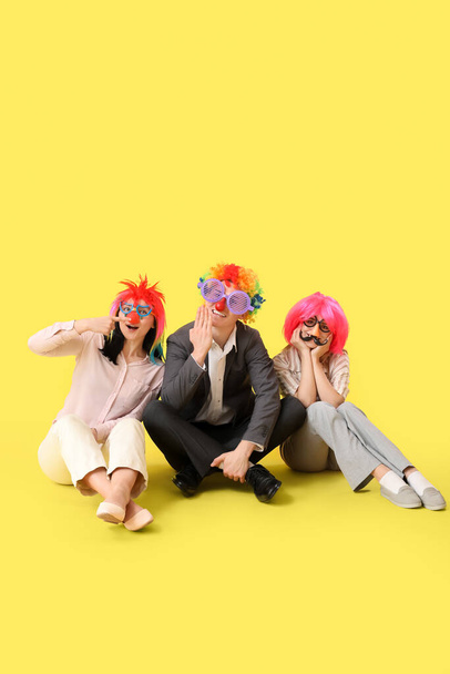 Деловые люди в смешной маскировке сидят на жёлтом фоне. Праздник Дня дураков - Фото, изображение