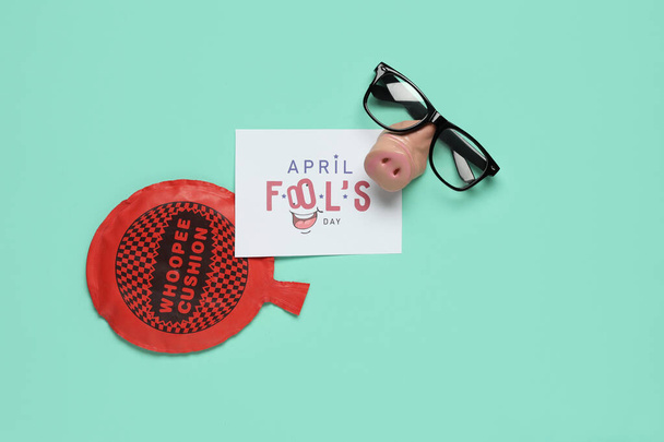 Carte postale festive pour April Fools Day avec des lunettes drôles et un coussin coqueluche sur fond turquoise - Photo, image