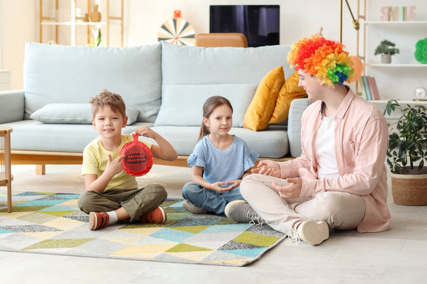 Padre en peluca de payaso colorido y sus hijos con cojín de whoopee en casa. Broma del Día de los Inocentes - Foto, Imagen
