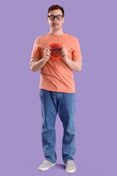 Junger Mann in lustiger Verkleidung mit Kissen auf fliederfarbenem Hintergrund. Feier zum Aprilscherz - Foto, Bild