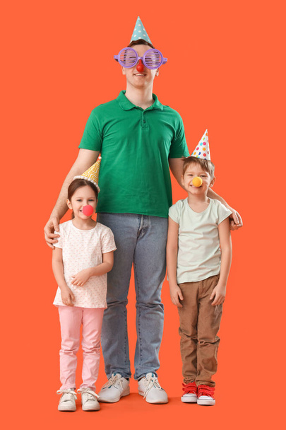 Father and his little children with funny disguises on orange background. April Fool's Day celebration - Photo, Image