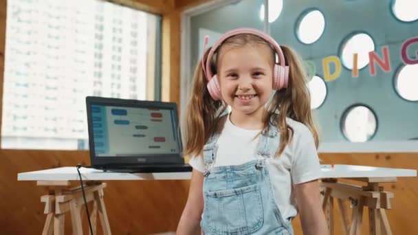 Nettes kaukasisches Mädchen lächelt in die Kamera, während Laptop Codierbildschirm zeigt. Ziemlich intelligentes Kind mit Laptop und Kopfhörer, um Ingenieur-Projekt zu studieren, prompt in der MINT-Ausbildung. Kreativ. Erution. - Filmmaterial, Video