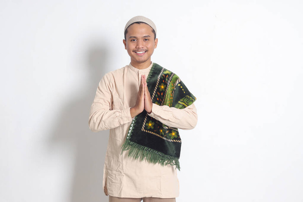 Портрет привабливого азіатського мусульманського чоловіка в сорочці з молитовним килимком, що показує вибачення та вітальний жест рук. Вибачтеся під час Ід Мубарака. Ізольоване зображення на білому тлі - Фото, зображення