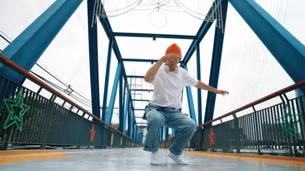 Un danseur de pause professionnel exécute des pas de danse de rue au pont. Asiatique hipster porter casque lors de la pose de gel. Break dancer, street dancer freestyle concept. Sport de plein air 2024. Brillamment. - Séquence, vidéo