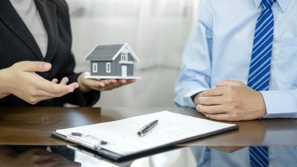Un agent immobilier avec un modèle de maison parle aux clients de l'achat d'assurance habitation. Concept d'assurance habitation. - Photo, image