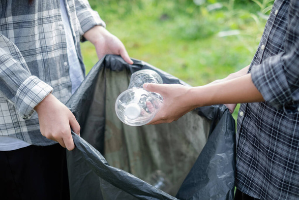 συλλογή απορριμμάτων, εθελοντική ομάδα μαζεύει πλαστικά μπουκάλια, βάζει σκουπίδια σε μαύρες σακούλες σκουπιδιών για να καθαρίσει στα πάρκα, να αποφύγει τη ρύπανση, να είναι φιλική προς το περιβάλλον και το οικοσύστημα. - Φωτογραφία, εικόνα