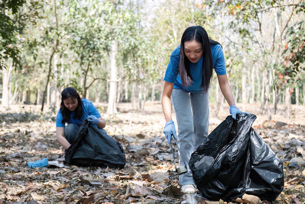 A group of Asian volunteers collects trash in plastic bags and cleaning areas in the forest to preserve the natural ecosystem.. - Foto, Imagen