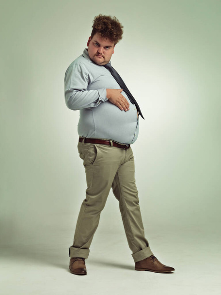 Business man, portrait and plus size with stomach gesture and silly in a studio with funny joke. Goofy, employee and office fashion with fun and work clothing with green background and humor. - Photo, Image