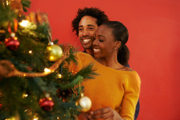 Ζευγάρι, Χριστούγεννα και διακόσμηση δέντρο στο σπίτι με ευτυχία για διακοπές γιορτή, δίνοντας ή δένοντας. Άνδρας, γυναίκα και χαμόγελο με φωτισμό για τη χειμερινή περίοδο για οικογενειακή εκδήλωση, αγκαλιά ή σαλόνι. - Φωτογραφία, εικόνα