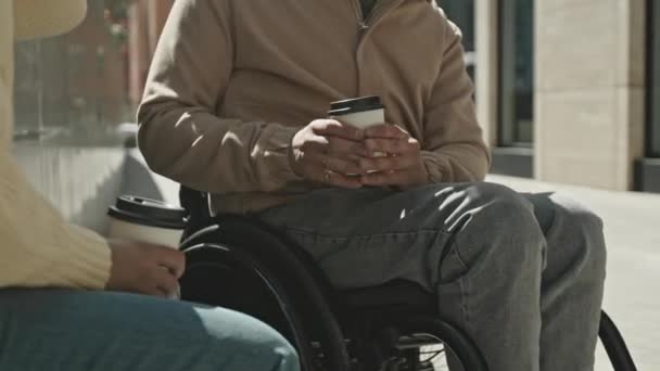 Naklonit se záběr muže na invalidním vozíku pití kávy z jít pohár a mluvit s přítelem při setkání venku ve městě - Záběry, video