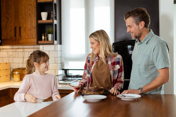 Een hartverwarmende scène ontvouwt zich als een familie geniet van een heerlijke chocoladetaart samen in de warmte van hun zonovergoten keuken, het delen van glimlachen en het creëren van herinneringen - Foto, afbeelding