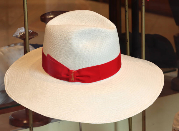 Bir mağaza vitrininde kırmızı kurdeleli şık beyaz fötr şapka - Fotoğraf, Görsel
