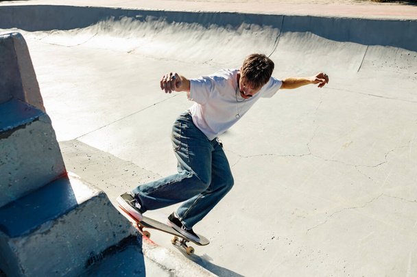 Aktywny młodzieniec jeżdżący na deskorolce w skateparku w słoneczny dzień. Koncepcja sportów ekstremalnych - Zdjęcie, obraz
