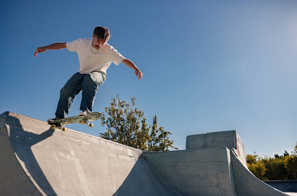 Active skateboarder jumping and performing a trick in a ramp of a skate park - 写真・画像