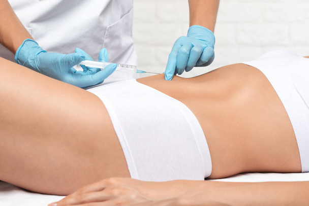 cosmetologist makes lipolytic injections to burn fat on the stomach and waist of a woman. Female aesthetic cosmetology in a beauty salon.Cosmetology concept. - Photo, Image