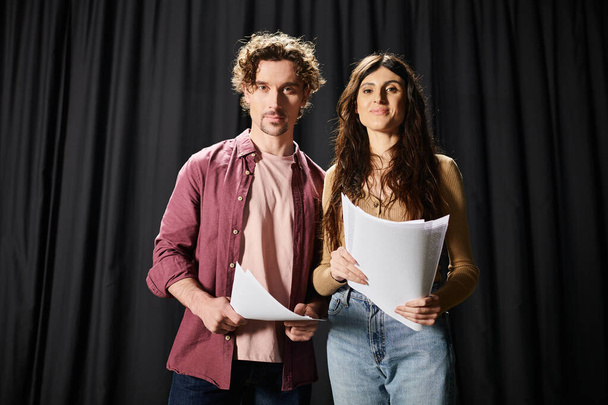 Симпатичный мужчина стоит рядом с женщиной, держащей лист бумаги во время репетиций в театре. - Фото, изображение