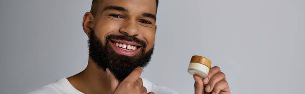 Handsome man with a beard holding a container of cream. - Photo, Image