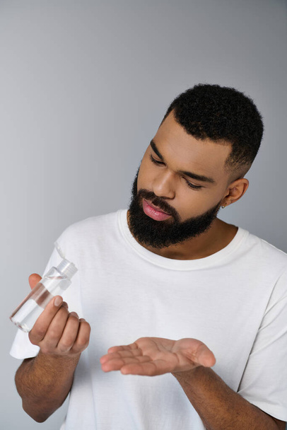 Um homem elegante com uma barba segura cuidadosamente um produto de preparação em suas mãos. - Foto, Imagem