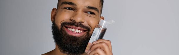 African american handsome man with a beard applying locion on his face. - Photo, Image