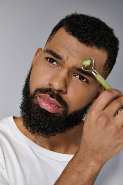 African american bearded man using face roller a for skincare routine. - Photo, Image