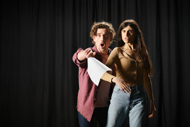 Un hombre y una mujer con estilo posan con confianza frente a una cortina negra durante los ensayos de teatro. - Foto, Imagen