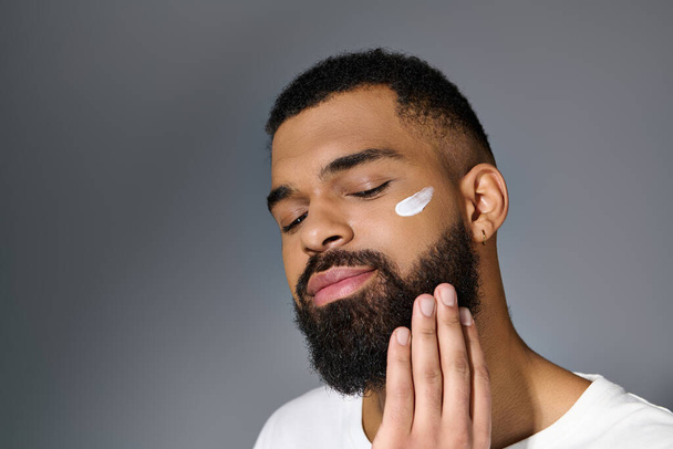 jovem afro-americano com uma barba mostrando creme branco em seu rosto. - Foto, Imagem
