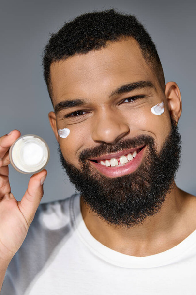 Handsome young man with a beard holding a jar of cream. - Photo, Image