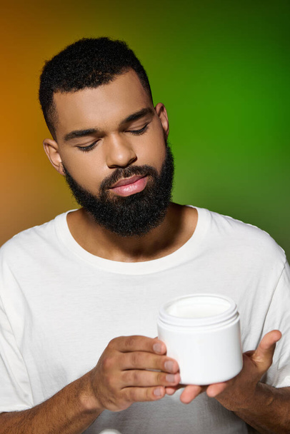 hombre guapo afroamericano con barba sostiene tarro de crema. - Foto, Imagen