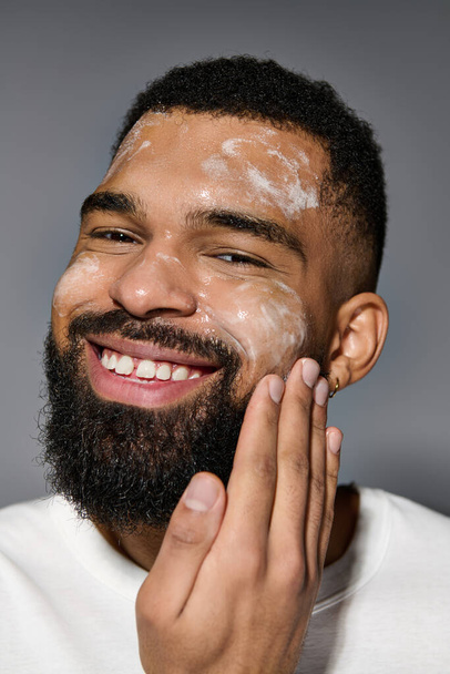 Appealing man with beard in white t-shirt, focusing on skincare routine. - Photo, Image