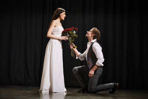 Egy férfi letérdel egy nő mellett, virággal a kezében egy színházi próbán.. - Fotó, kép