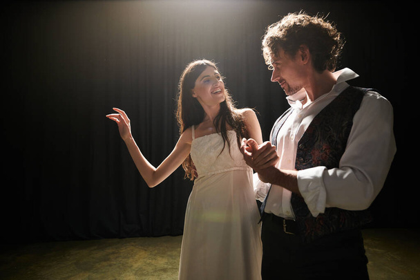 Una mujer con un vestido blanco y un hombre con un chaleco negro ensayan una actuación en un teatro. - Foto, imagen