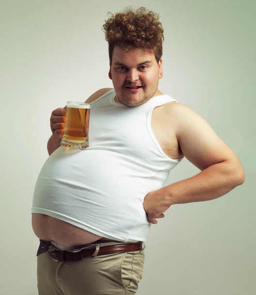 Obese, gewichtstoename en lager voor de man in de studio met drank voor ongezonde gewoonte, plus grootte en grap. Overgewicht persoon met glas op vette maag voor evenwicht, dronken en humor voor alcohol en komiek. - Foto, afbeelding