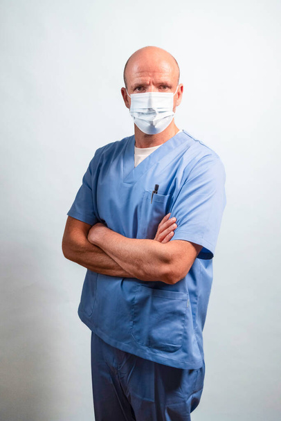 Portrait of a physiotherapist in light blue gown and face mask looking at camera in studio. - Photo, Image