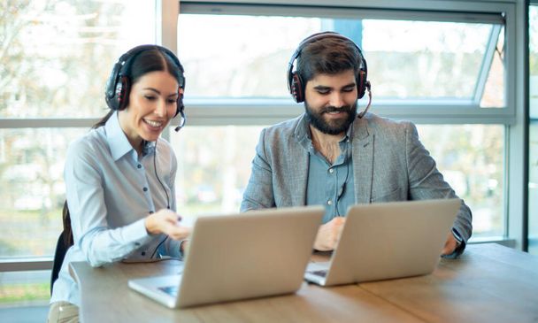 Mooie jonge man en vrouw telefonische operators met headsets praten met de klant op laptop in de klantenservice oproep support hulplijn. - Foto, afbeelding