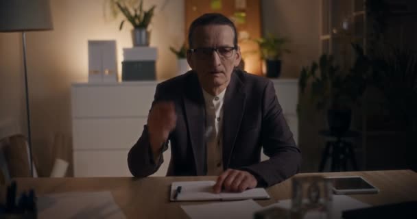 Retrato de triste gerente sênior do sexo masculino removendo óculos enquanto sentado na mesa no final da noite no escritório - Filmagem, Vídeo