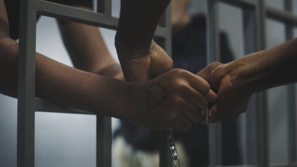 Wärter legt jungen Gefangenen Handschellen an. Multiethnische Teenager verbüßen ihre Haftstrafe in einer Justizvollzugsanstalt oder in einem Internierungslager. Junge Häftlinge in der Gefängniszelle. Justizsystem. Nahaufnahme. - Foto, Bild
