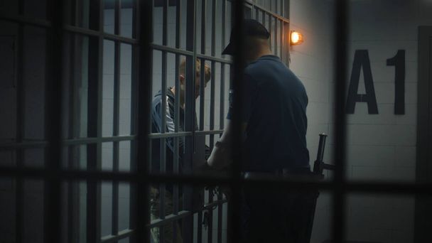 Wärter legt jungen Gefangenen Handschellen an. Teenager verbüßt Haftstrafe in Justizvollzugsanstalt oder Haftanstalt. Junger Häftling in Gefängniszelle. Justizsystem. Blick durch Metallstangen. - Foto, Bild