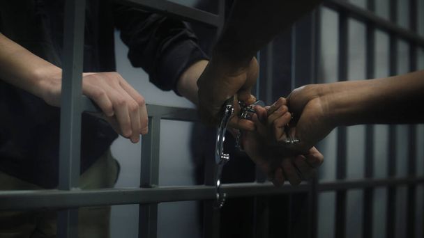 Warden takes off handcuffs from young prisoner. Multi ethnic teenagers serve imprisonment term in correctional facility or detention center. Young inmates in prison cell. Justice system. Close up. - Photo, Image
