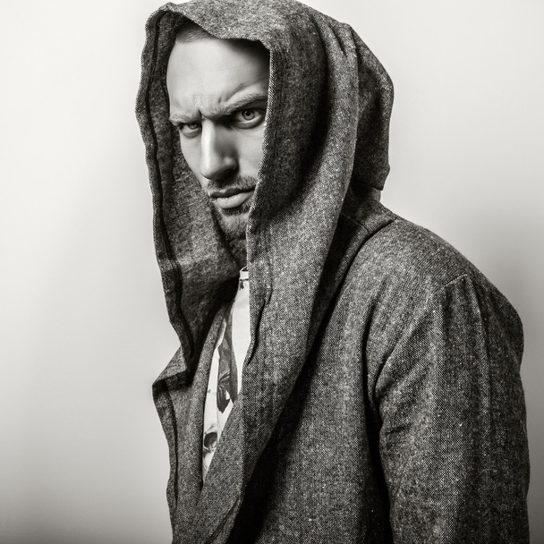 Studio portrait of young handsome man in casual cape with a hood. Close-up sepia photo. - Photo, Image
